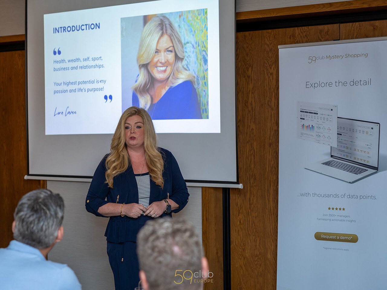 speaker in front of an audience with a powerpoint at the back